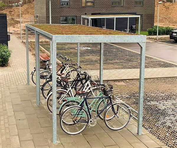 Casa 01 cykeloverdækning i galvaniseret stål med en række cykelstativer og et sedum tag