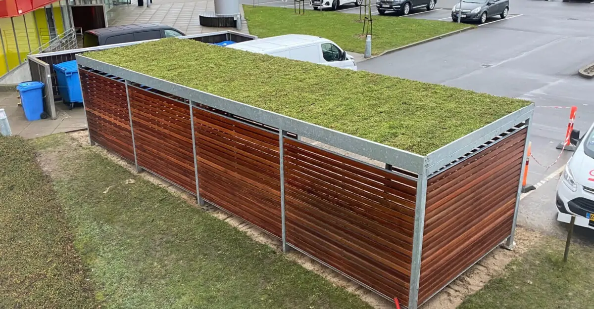 modulopbygget cykeloverdækning i galvaniseret stål med hårdttræ beklædning og sedum tag, som både fremstilles som cykelskur eller som overdækning til affaldscontainere