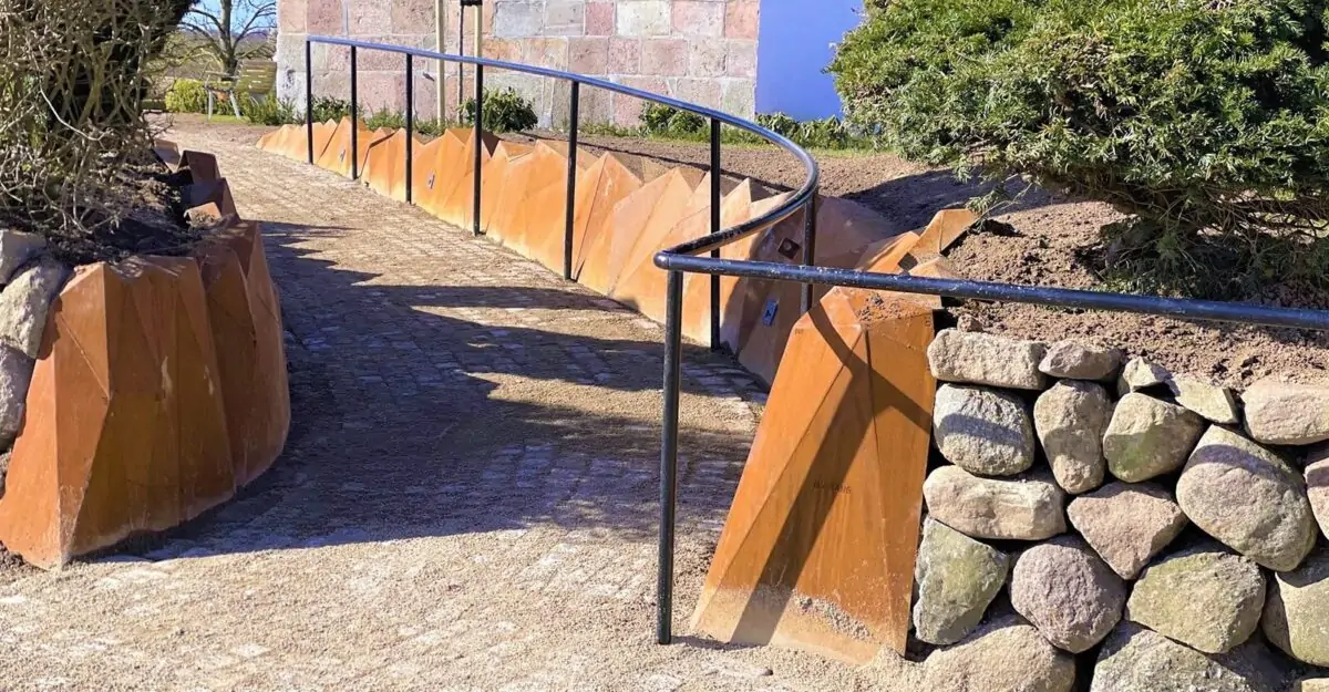 en usædvanlig stålkant af 452 forskellige trekant plade i 5 mm cortenstål, der er svejset som en stenvæg langs stien mod Elev Kirke