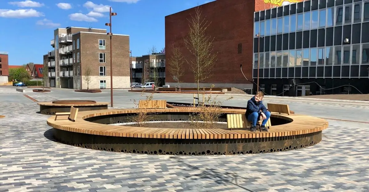 cirkelbænke i cortenstål beklædt med træ, med rygstøtte og specialdesignede huller i bunden, der er lavet til at lade regnvandet gå igennem og vande planterne