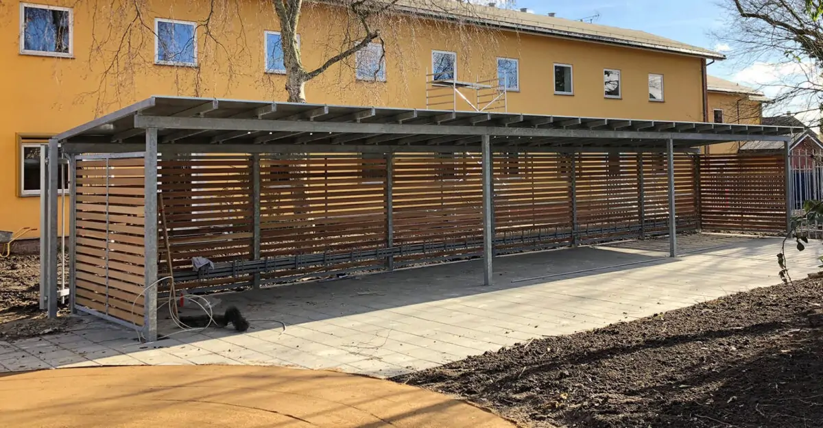 modulopbygget cykeloverdækning i galvaniseret stål med hårdttræ beklædning og zink tag, som både fremstilles som cykelskur eller som overdækning til affaldscontainere
